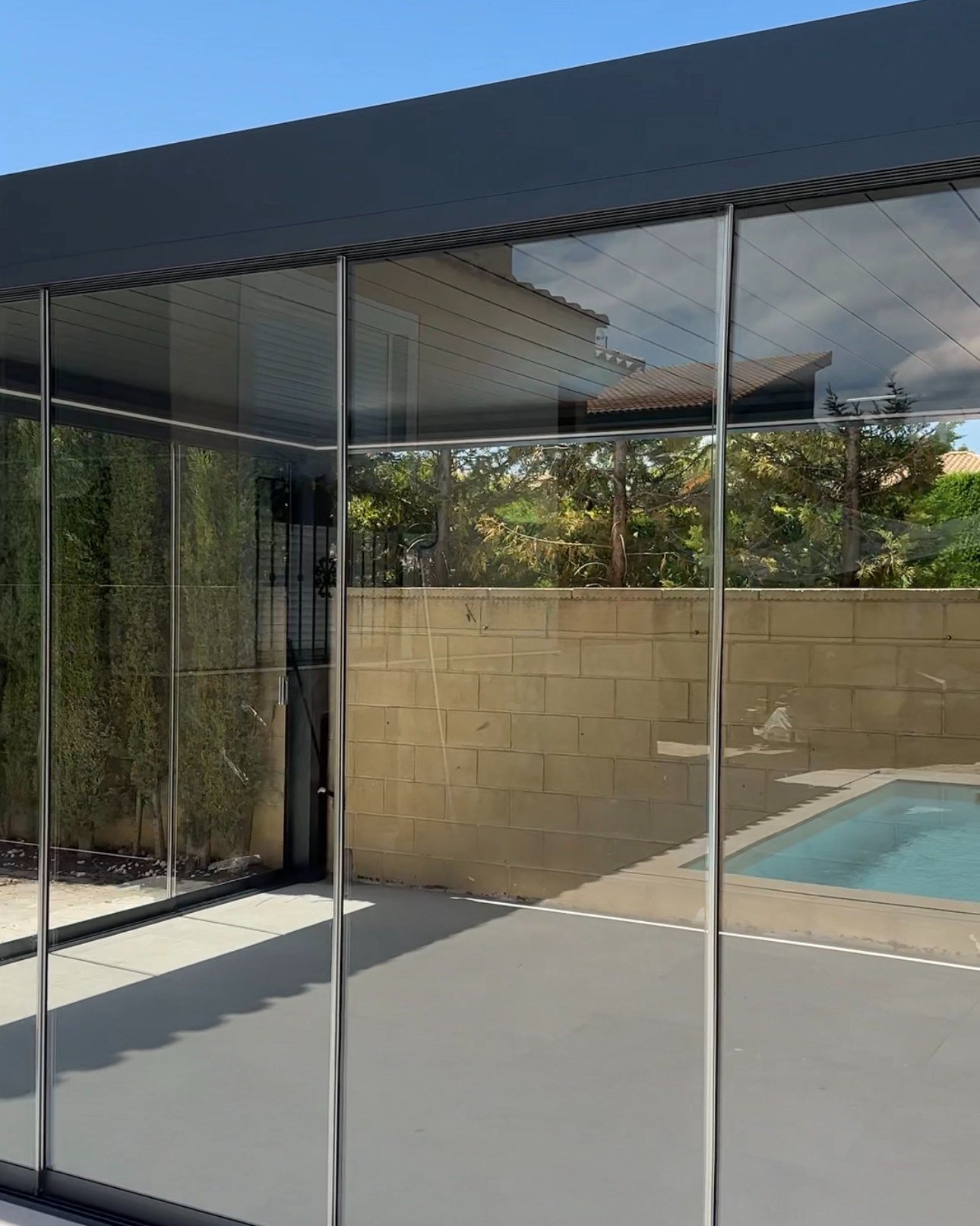 Pérgola bioclimática gris cerrada con cortinas de cristal junto a una piscina en Elche
