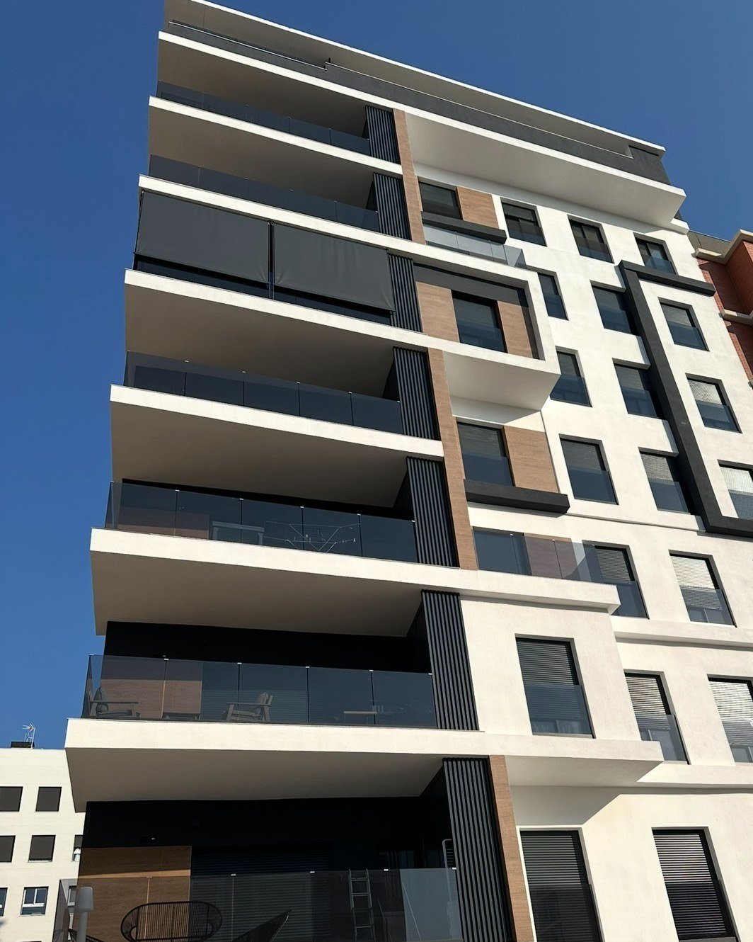 Fachada de un edificio nuevo de Elche con toldos verticales bajados en un balcón